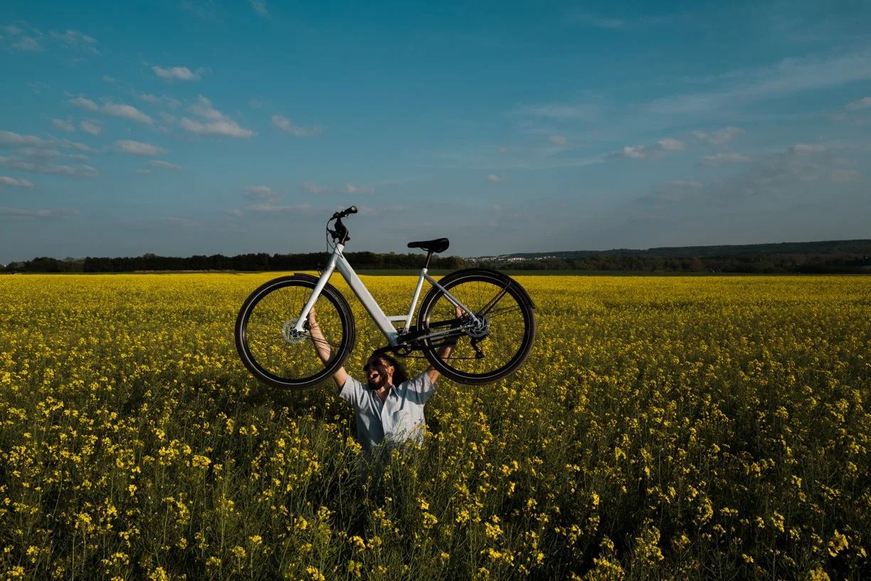 man holding up up way bike in flowery field