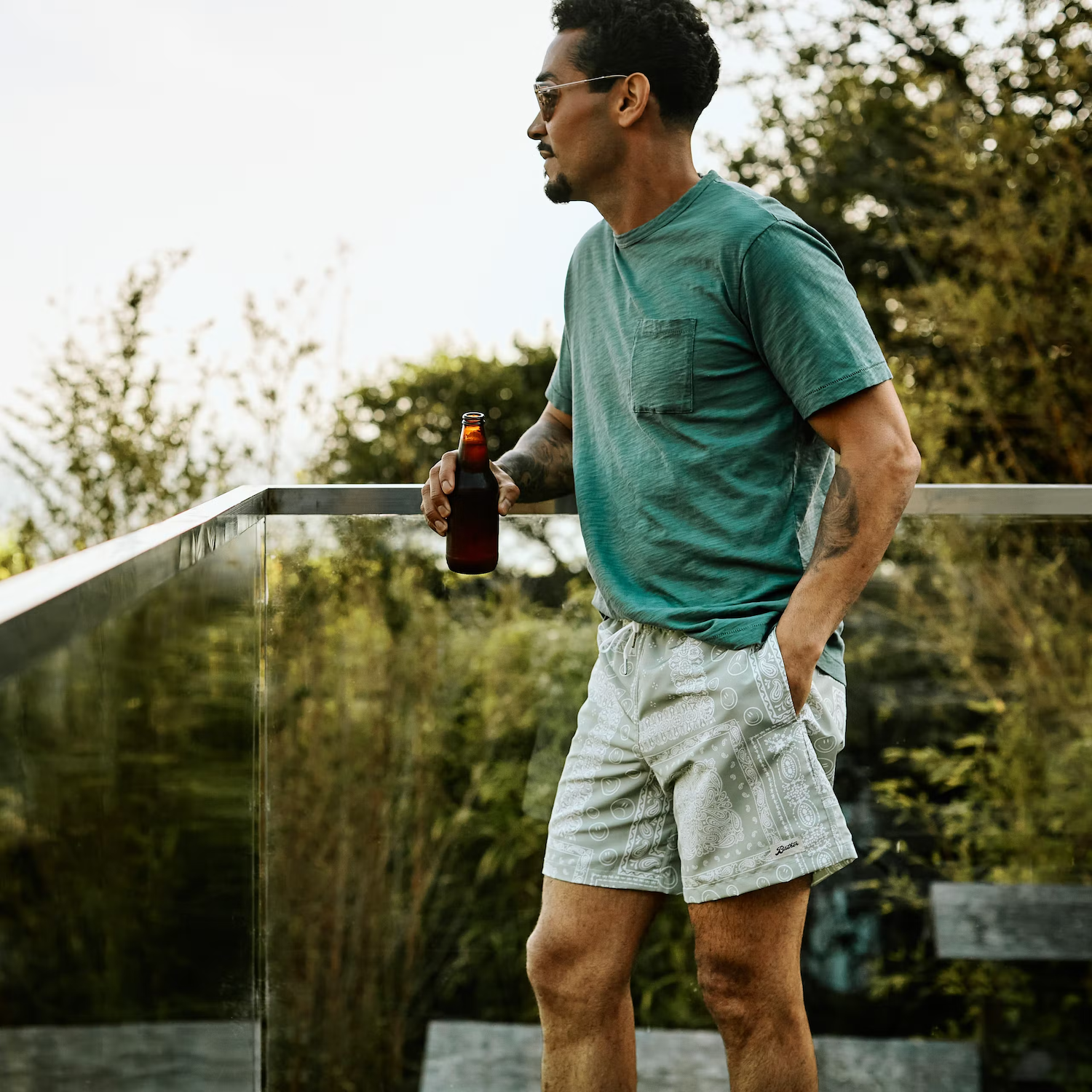 huckberry man standing on backyard deck drinking beer in bather trunk co bandana swim short