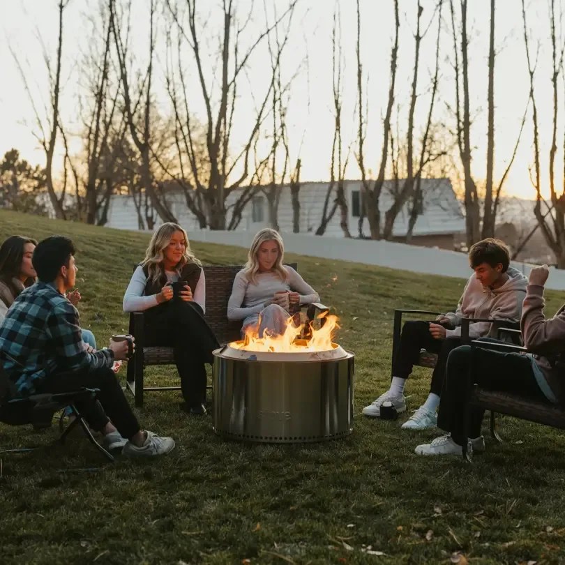Solo Stove Canyon firepit in backyard with six people sitting around it in chairs