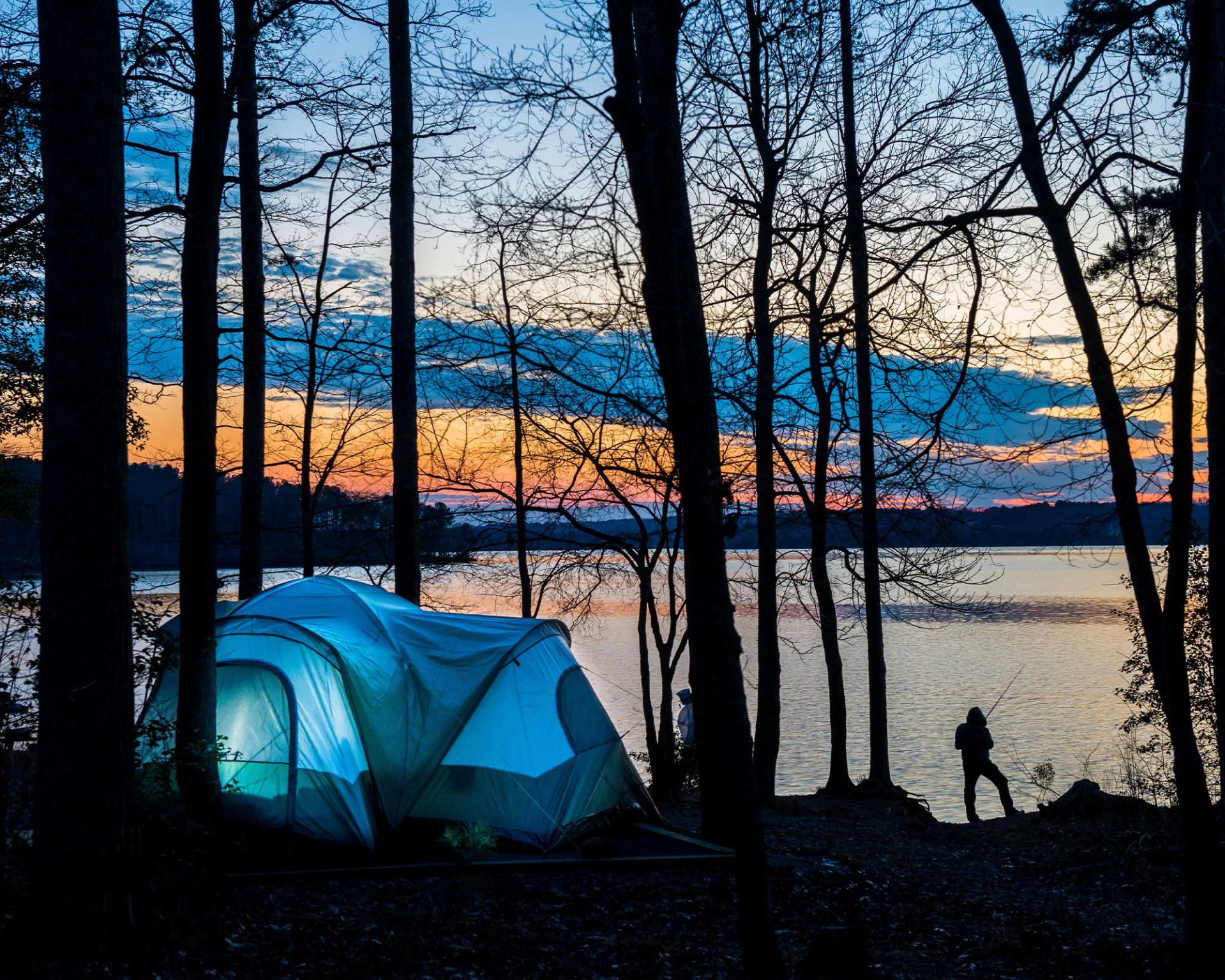 a person standing by his tent as the sun sets
