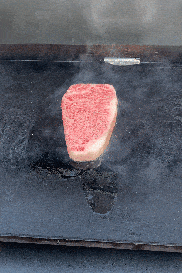 a steak cooking on a gas grill griddle