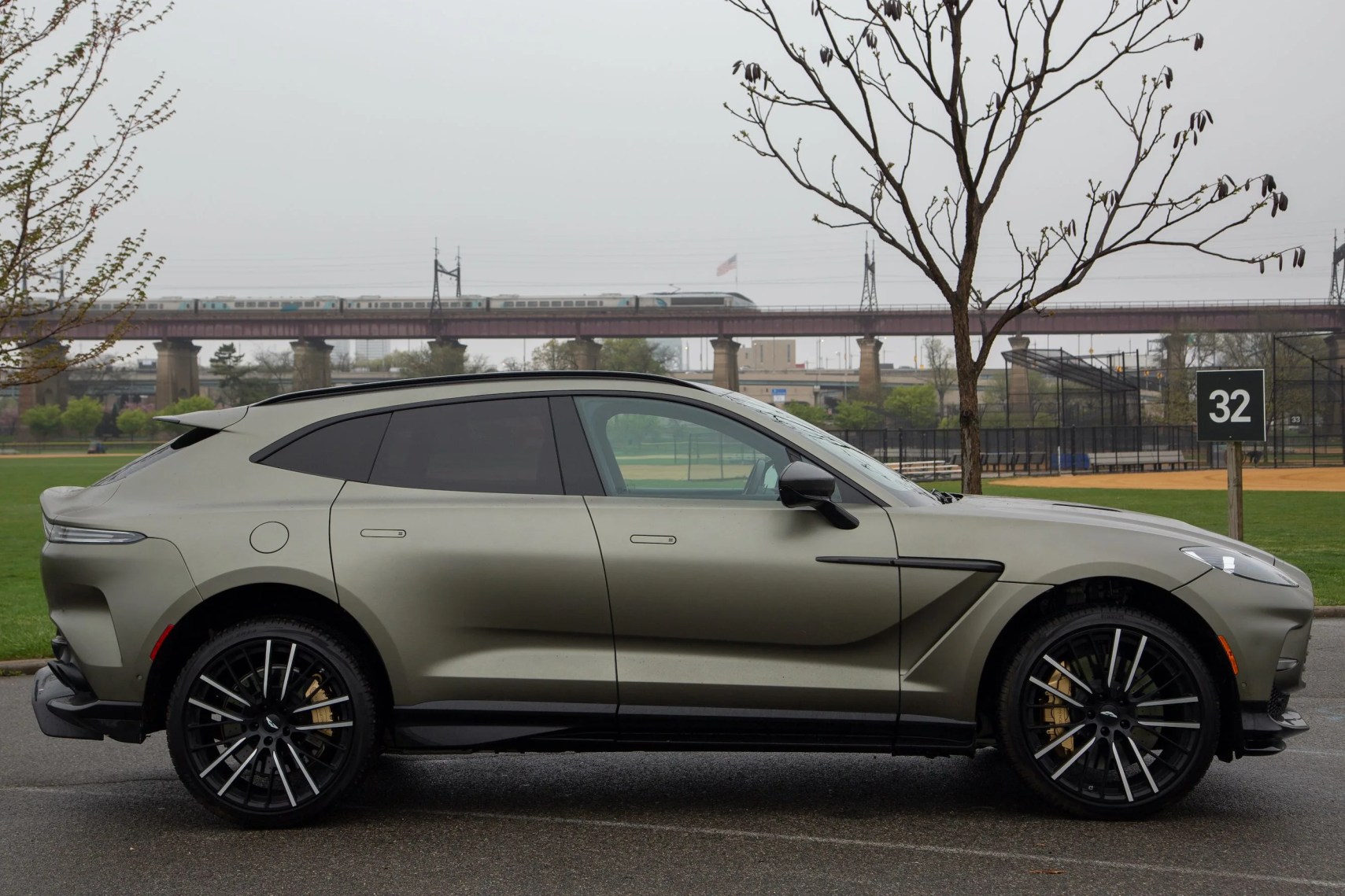 aston martin dbx 707 parked sideways as an amtrak acela train passes on a trestle in the distance