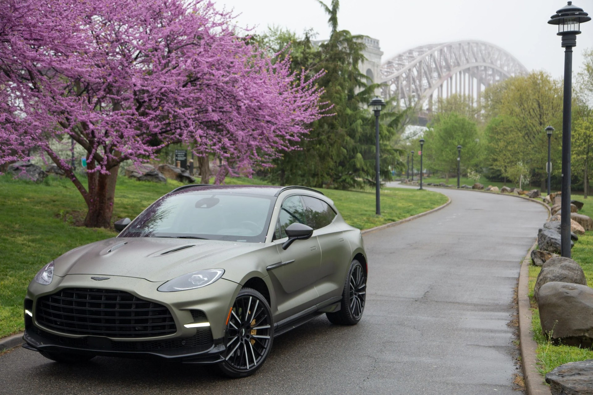 aston martin dbx 707 in green in front of a blossoming cherry tree with a curved bridge in the background