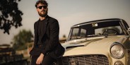 a man wearing sunglasses leaning against the hood of a car