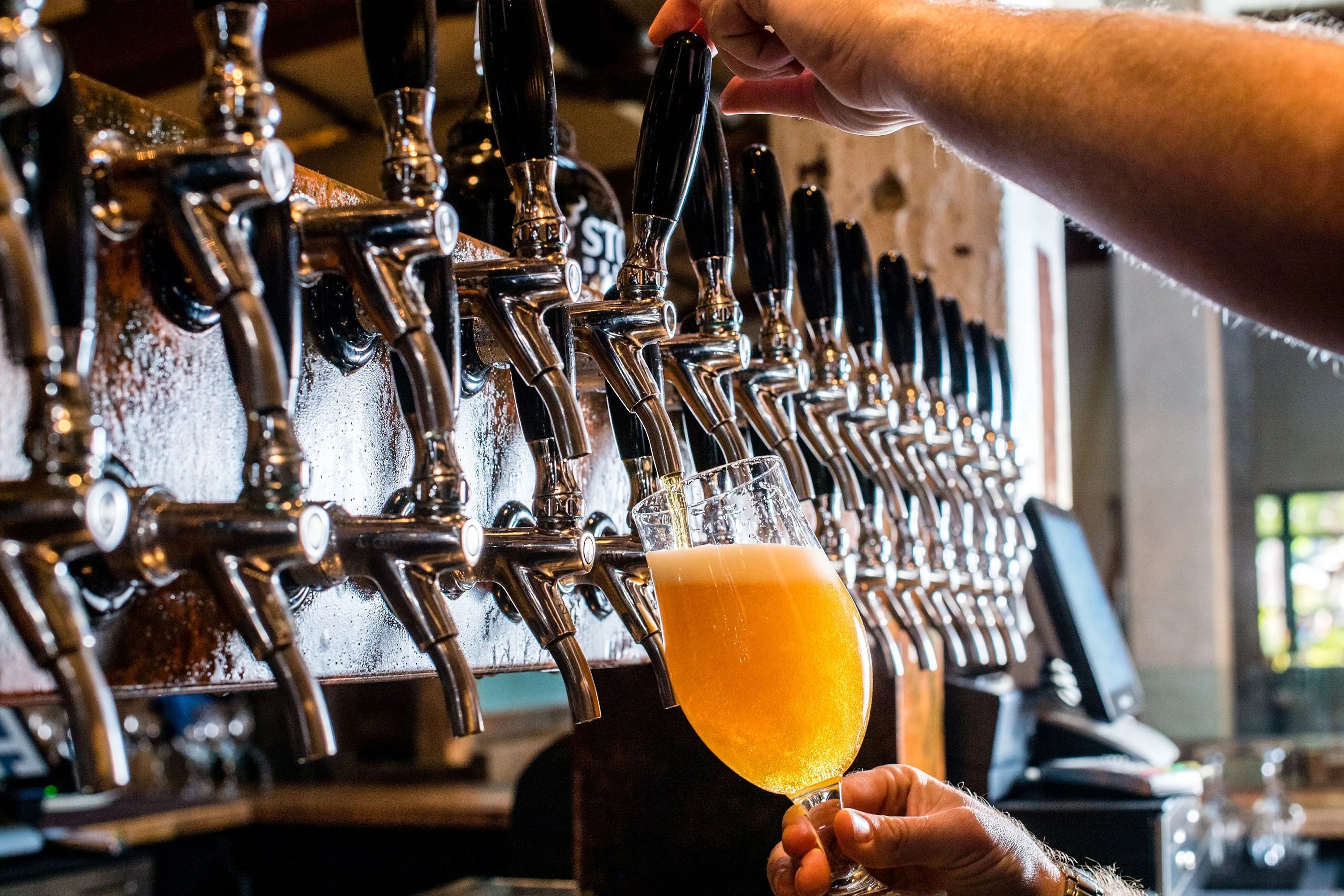a person pouring an ipa beer into a glass from a tap