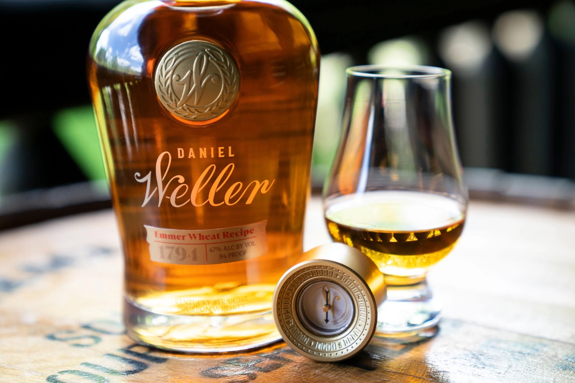 a bottle of daniel weller whiskey next to a glass on a barrell