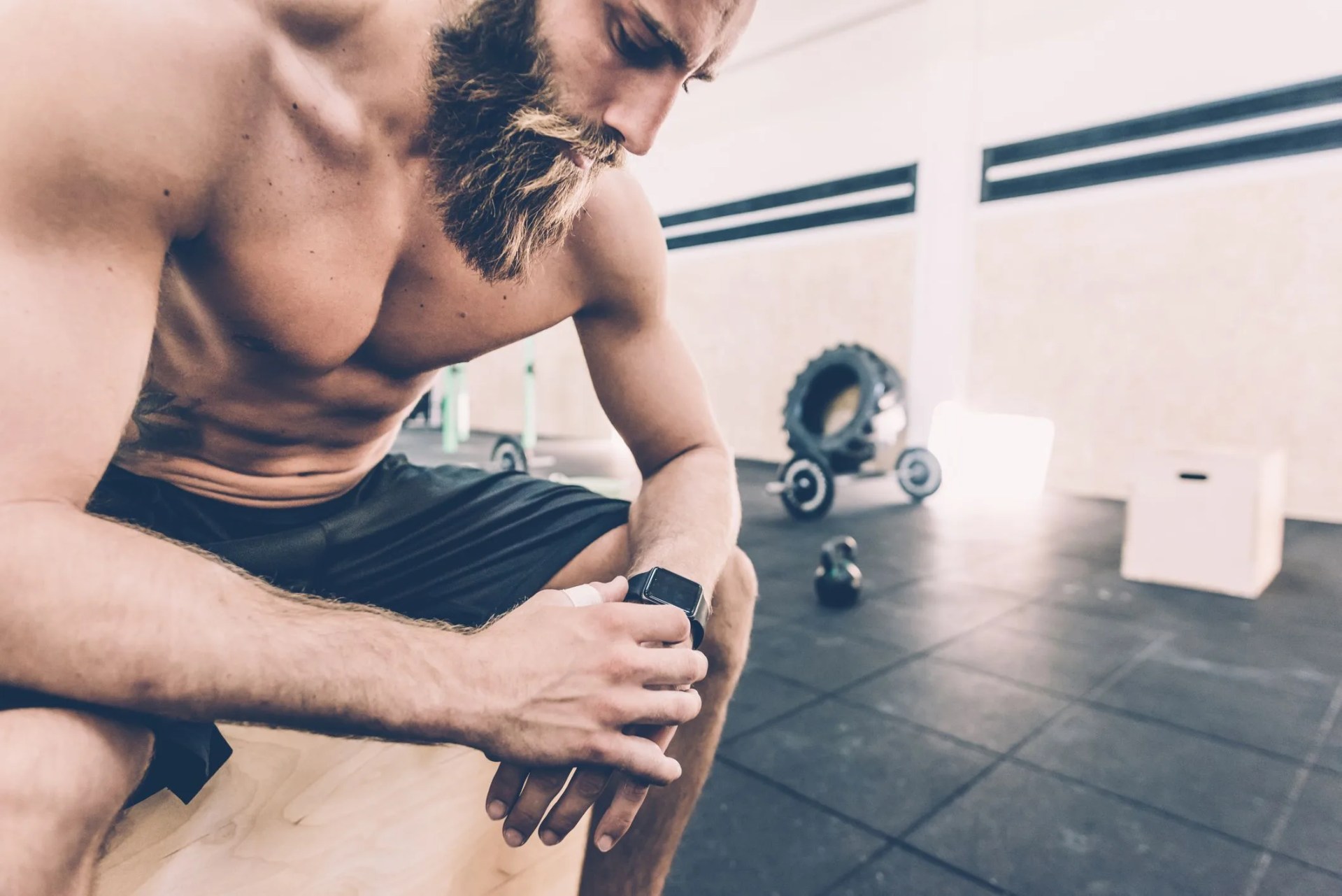 young man sitting checking smartwatch in cross training gym