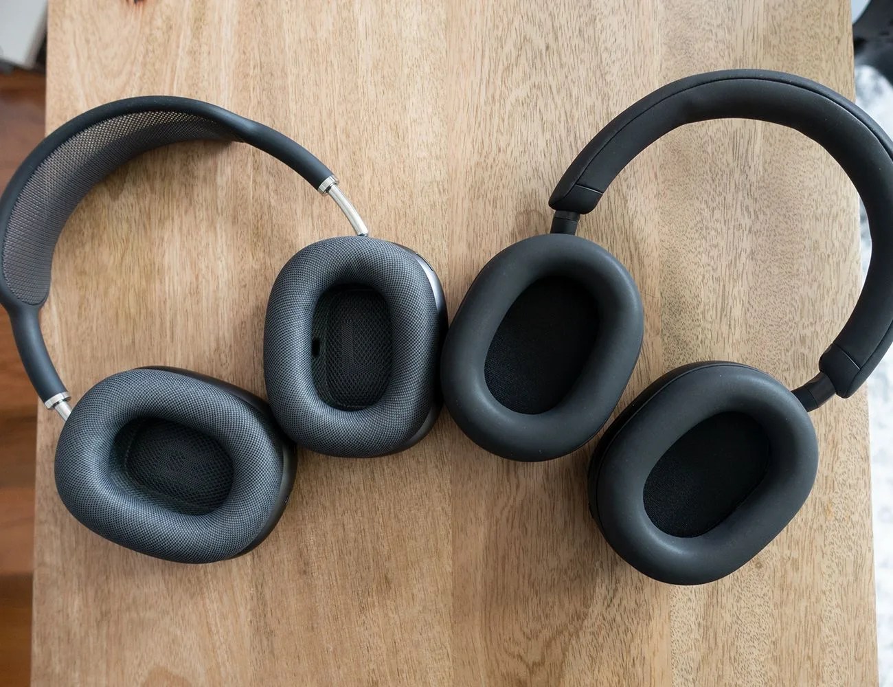 black sony wh 1000xm5 headphones and black apple airpod max headphones laying on a table showing the inner ear of the headphones
