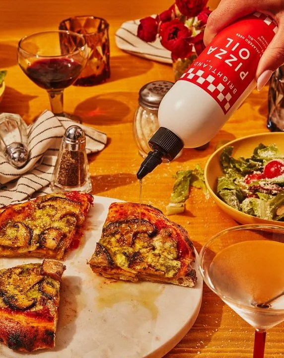 hand drizzling brightland pizza oil on pizza