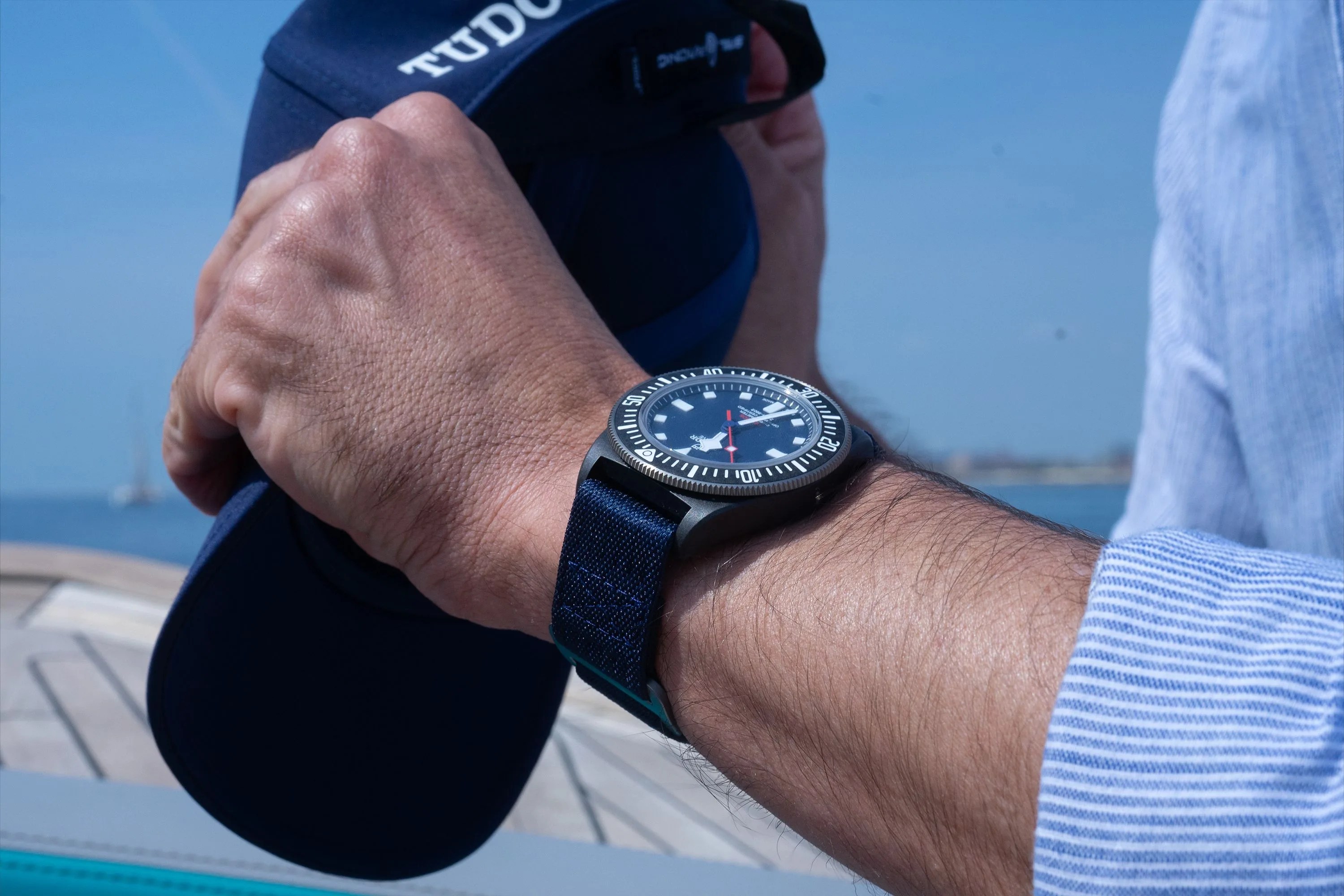 a man wearing a watch on a boat while holding a hat
