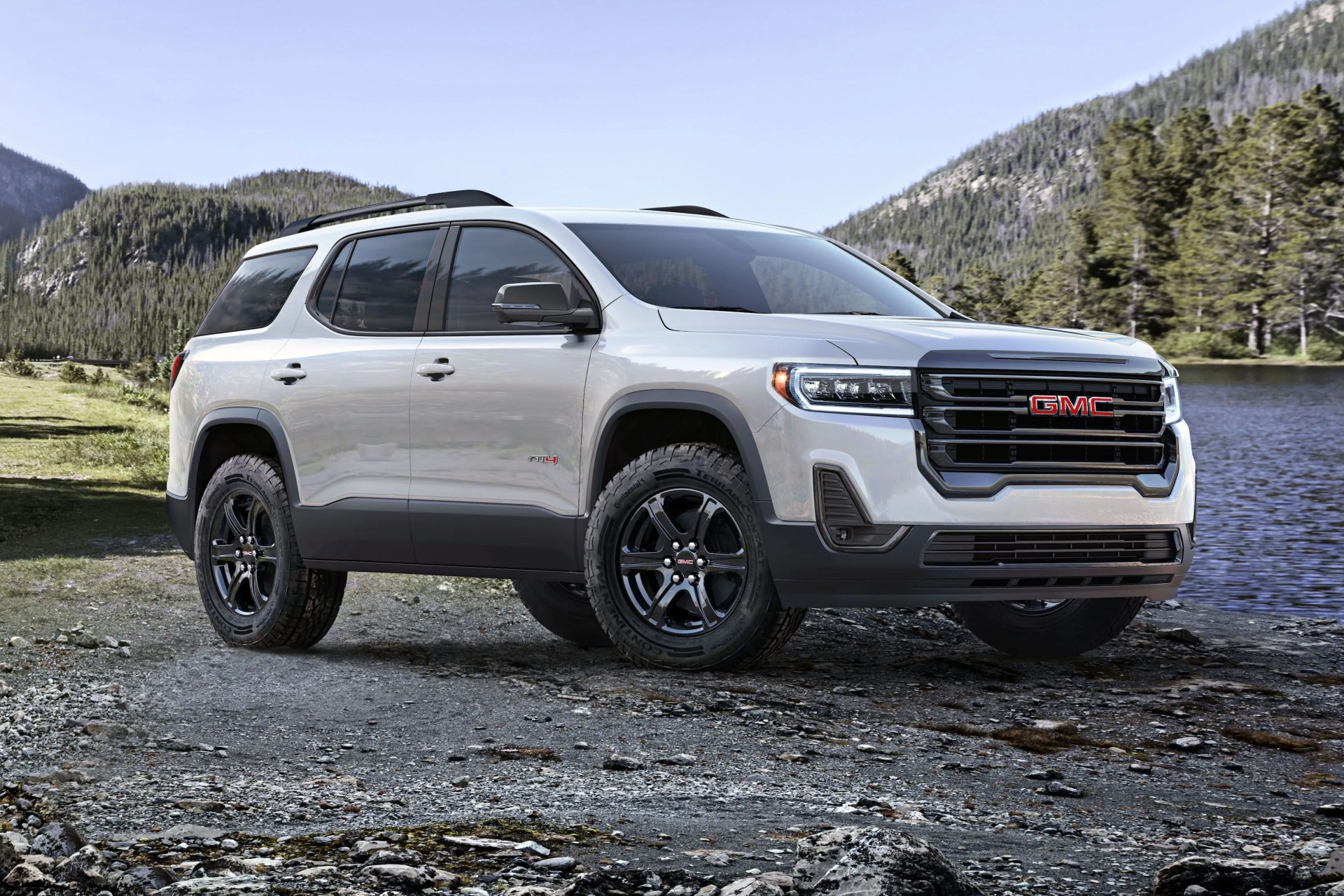 front driver 34 view of 2023 gmc acadia at4 in summit white with mountains and lake in background