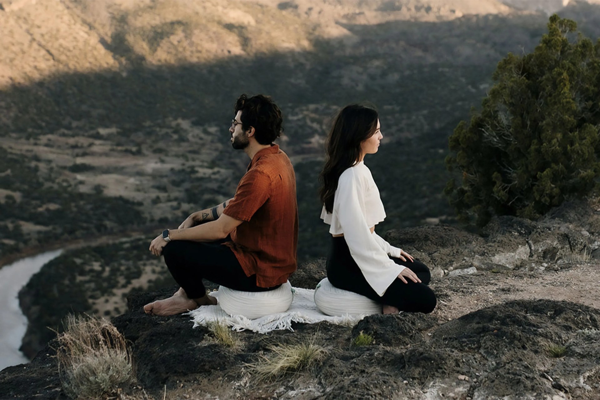 two people sitting on meditation cushions outside on a mountain