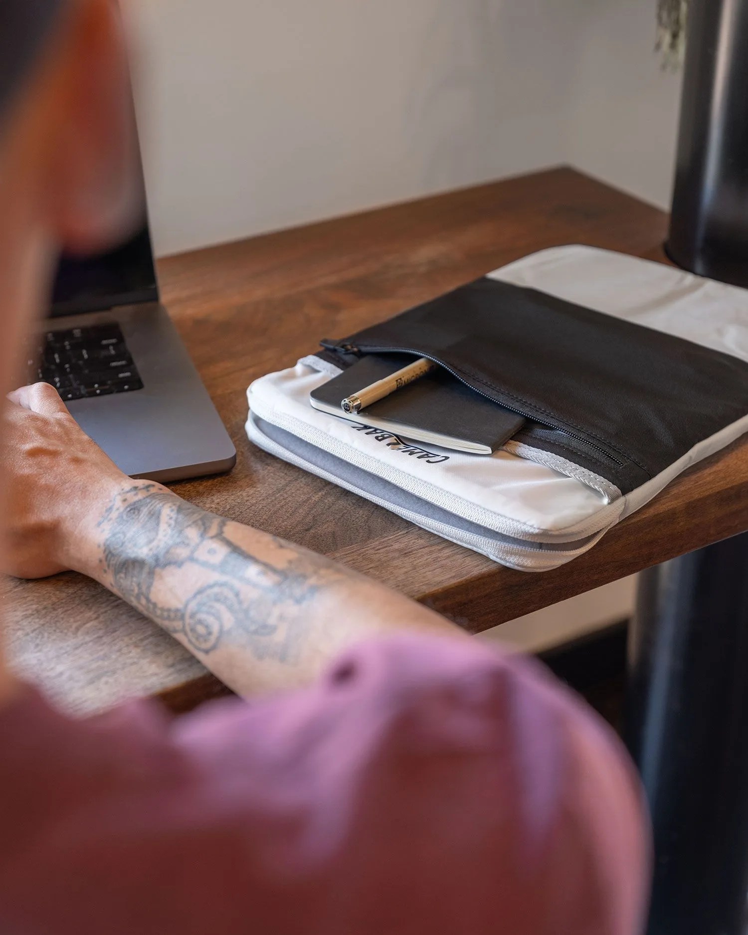 man using macbook with camelbak sleeve next to him on table
