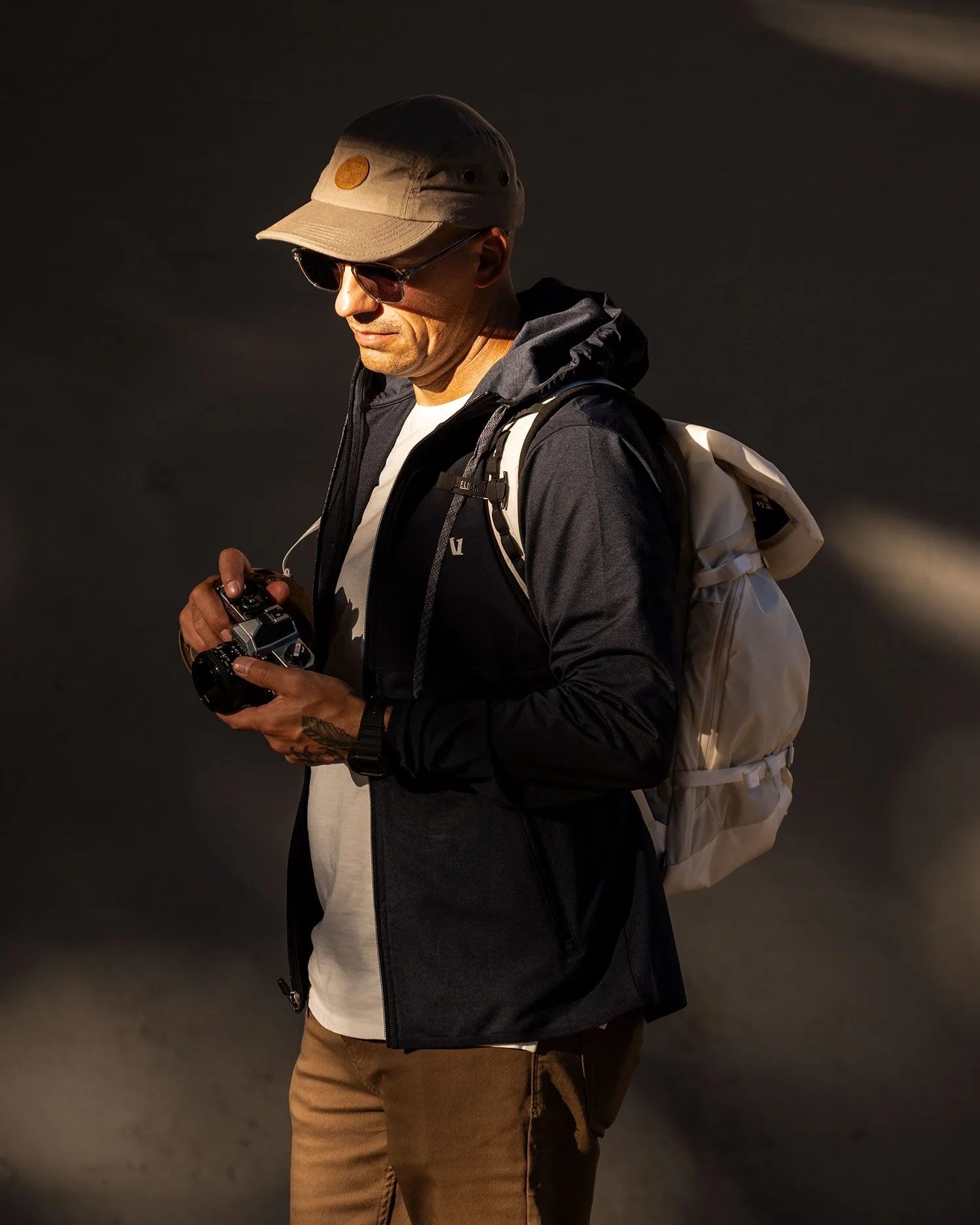 man wearing sunglasses holding camera while wearing white camelbak backpack