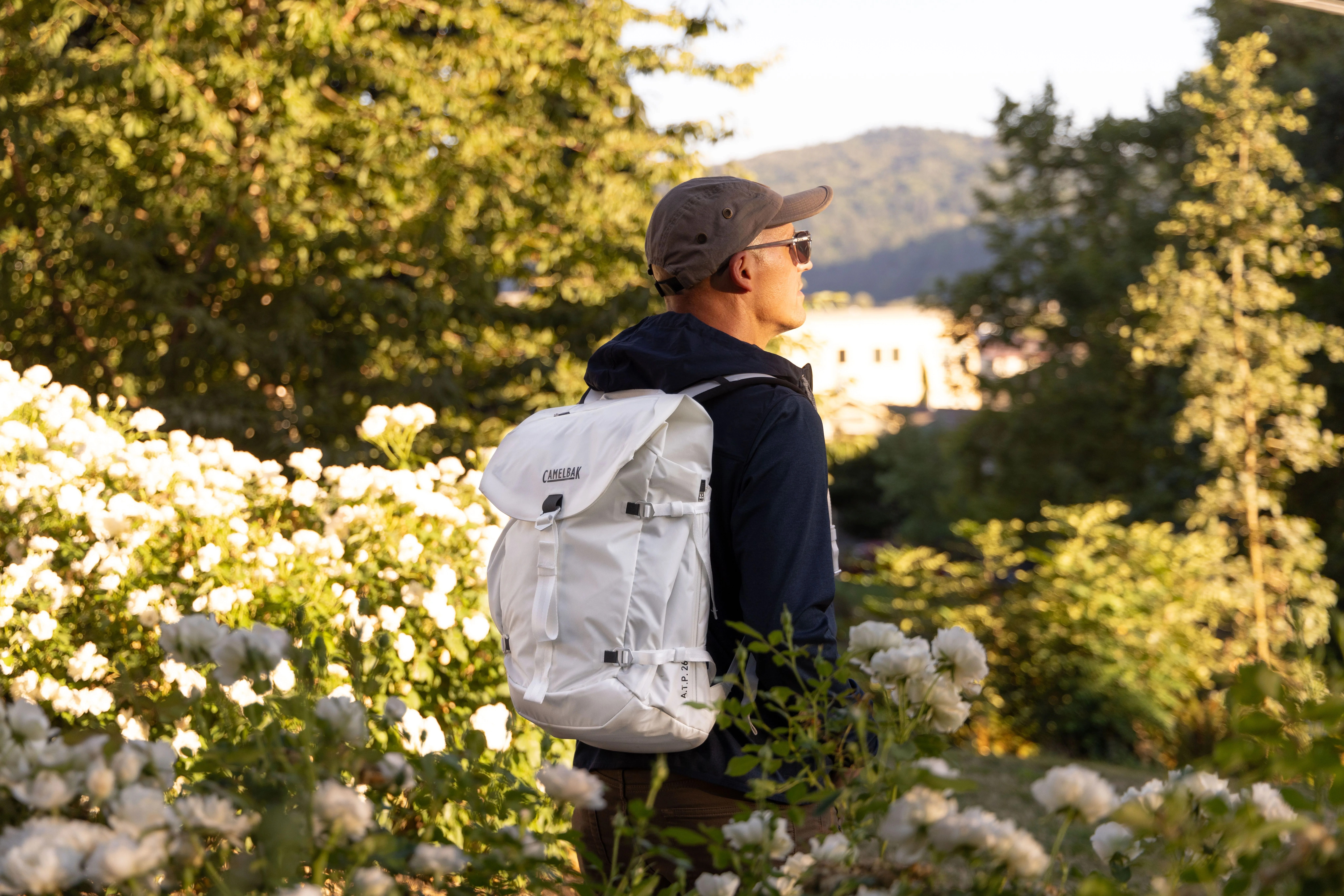 man standing by white flower bushes wearing white camelbak backpack