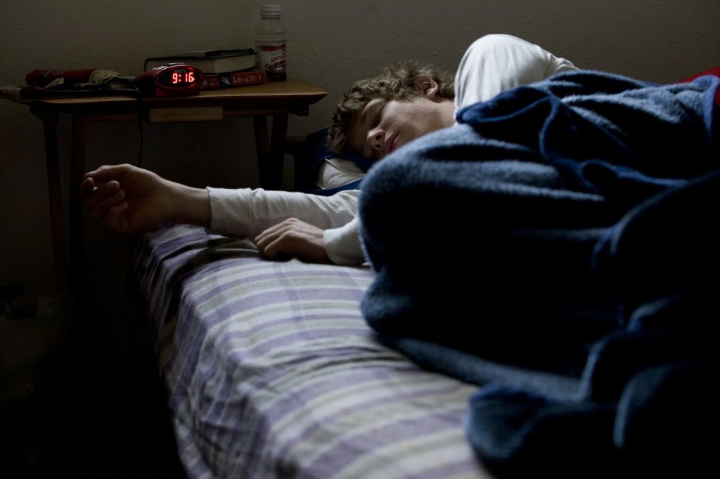 a young man snoozes in his room as his alarm clock reads 916 am
