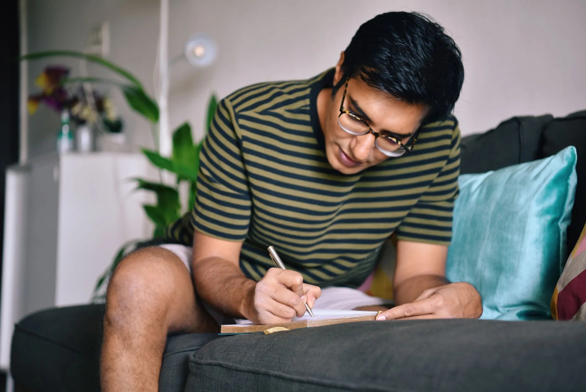 man writing in a diary sitting on a sofa