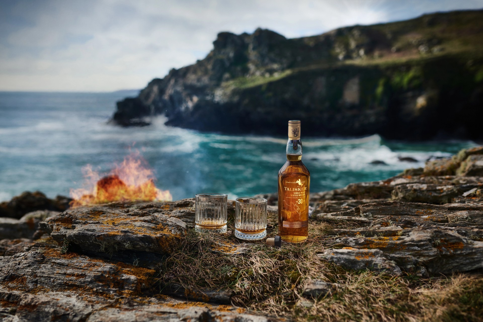 scotch whisky bottle and glasses next to the ocean