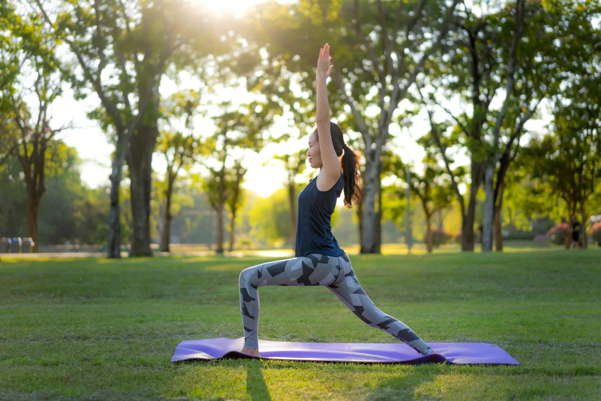 young asian woman practicing warrior 1 yoga in park at sunset