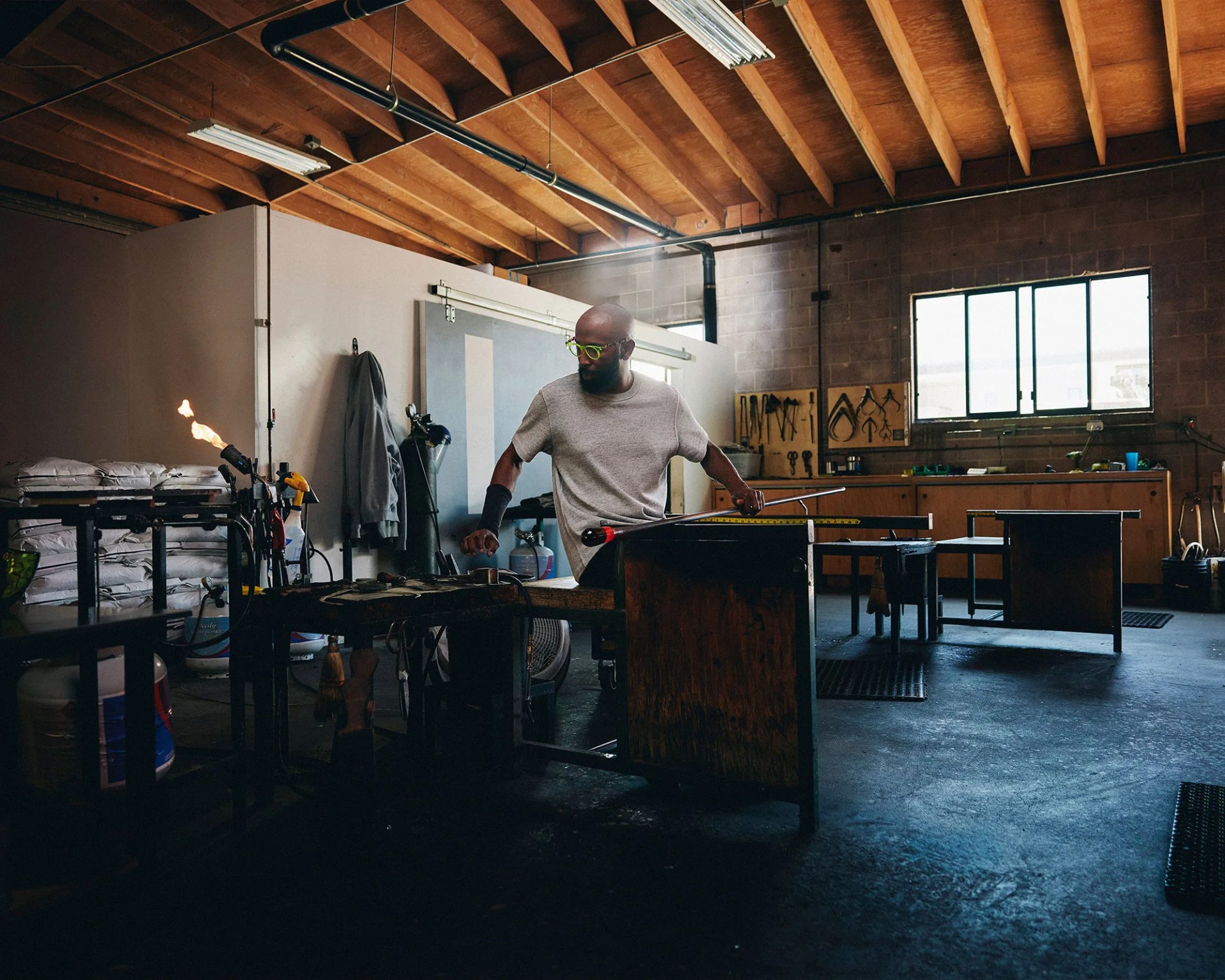 Cedric Mitchell sitting in his studio holding a metal rod with cooling glass