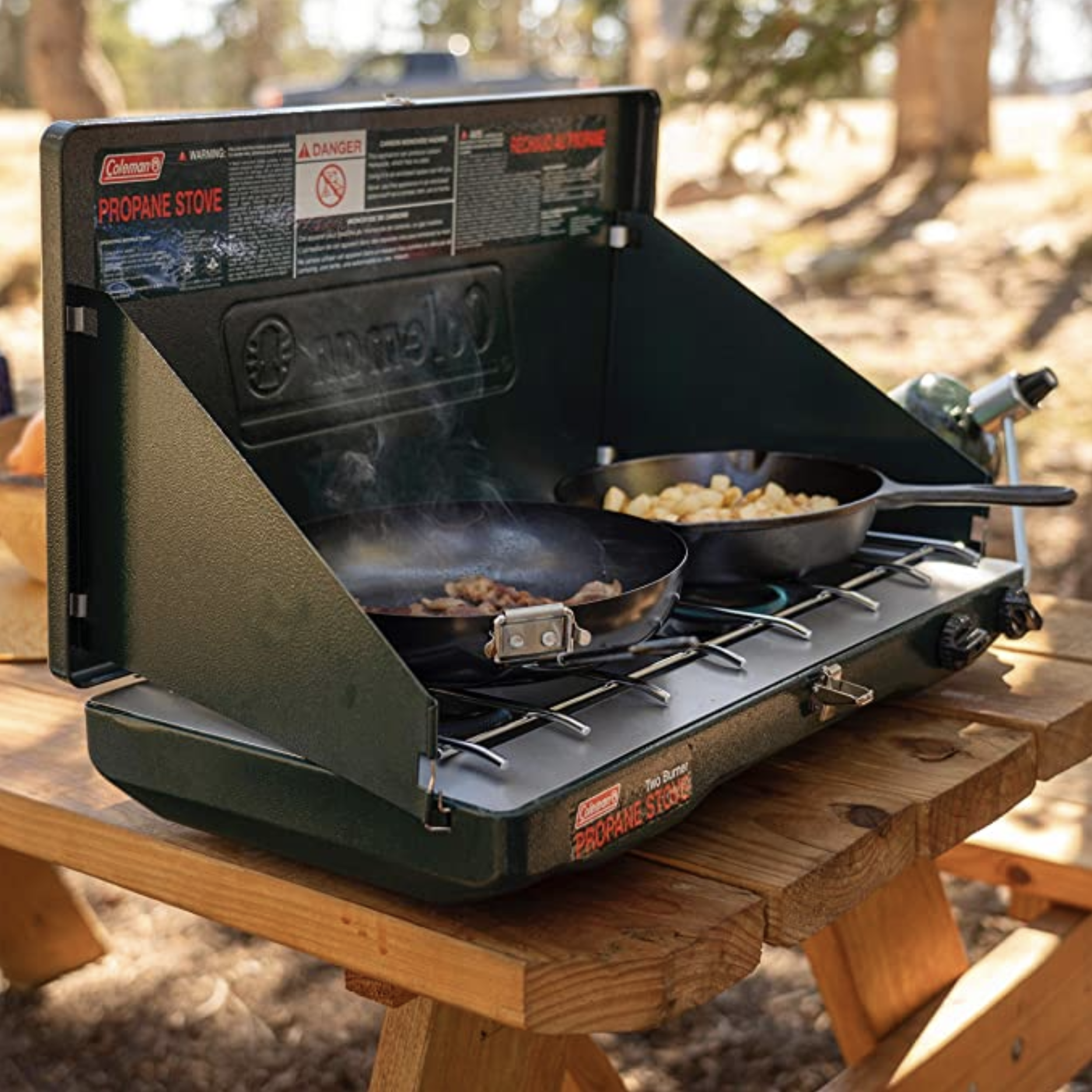 a camping stove with two pans cooking food on a picnic table