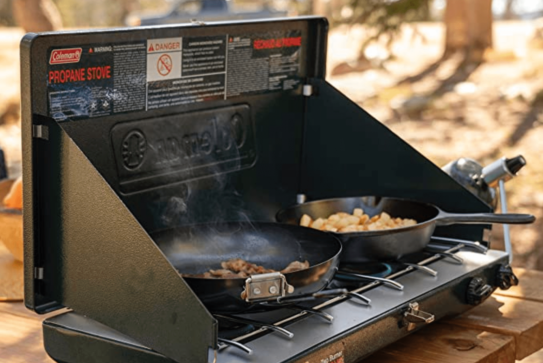 a camping stove with two pans cooking food on a picnic table