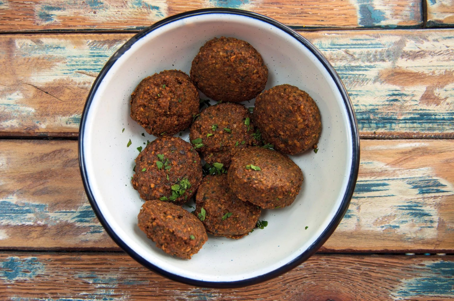 cooked falafel balls in an enameled tin bowl on a distressed recycled wood table top