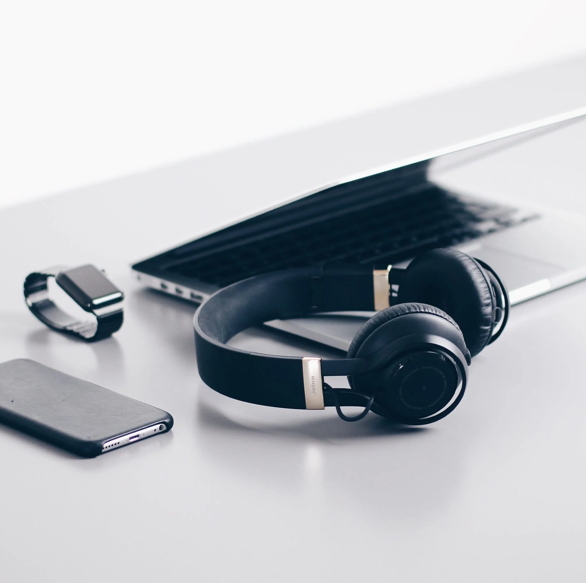 electronics on a white surface laptop, headphones, smart watch, and cell phone