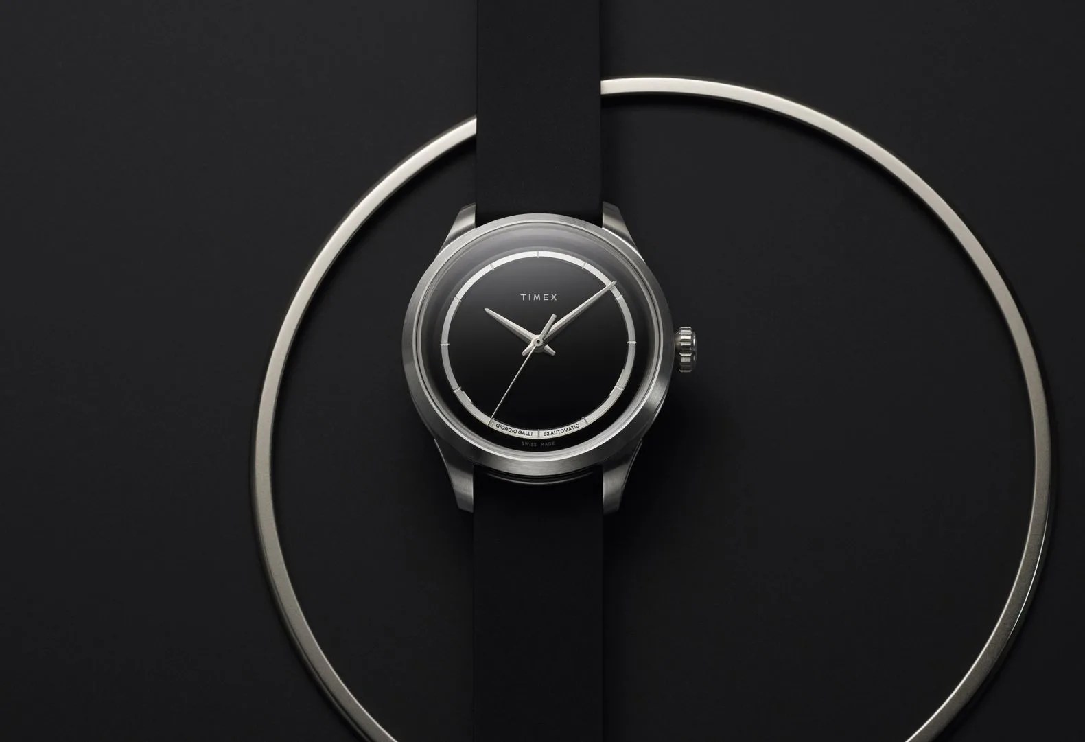 black and white image of a watch on a table and a large steel ring