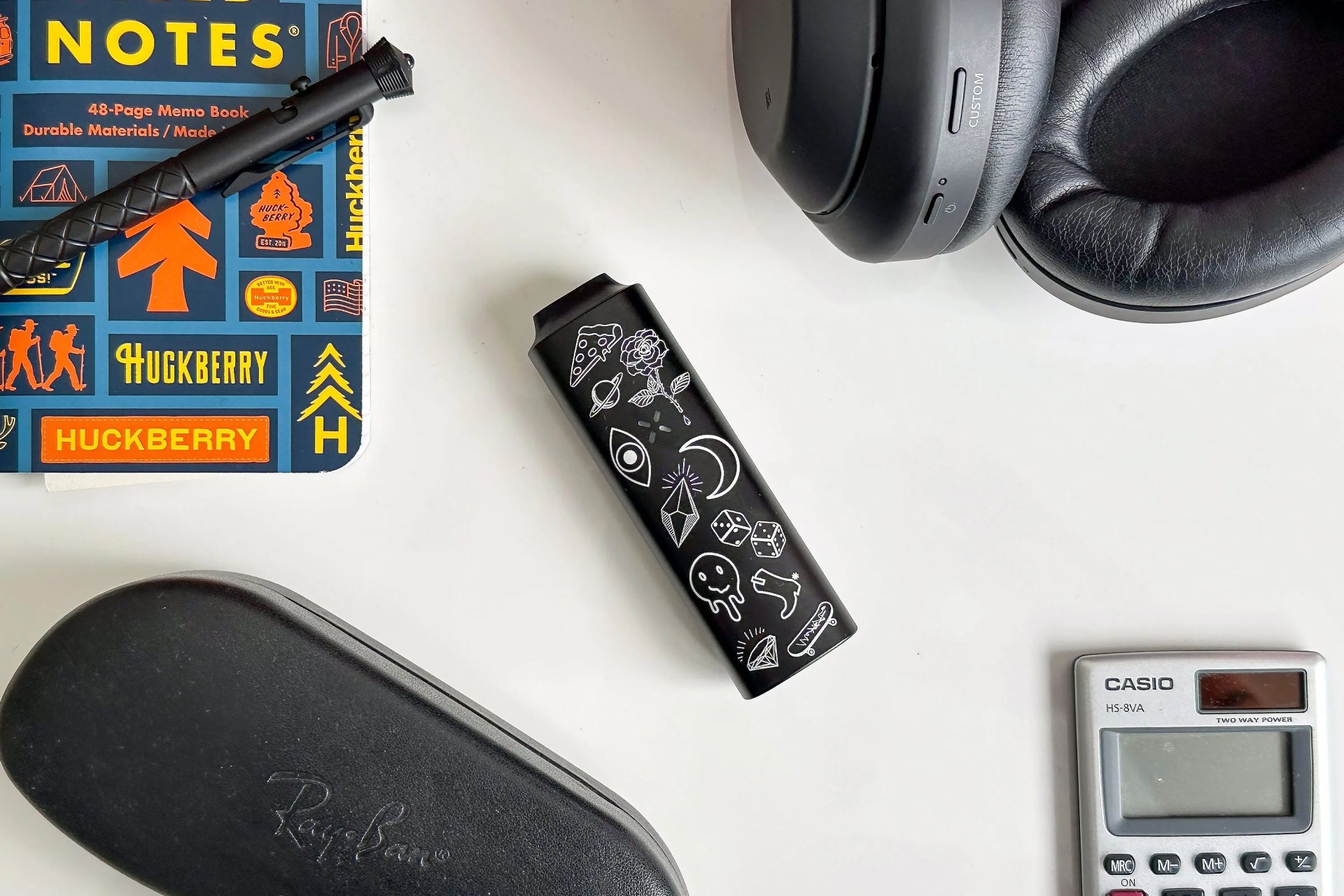pax mini on a table with a notebook, pen, glasses case, headphones, and calculator