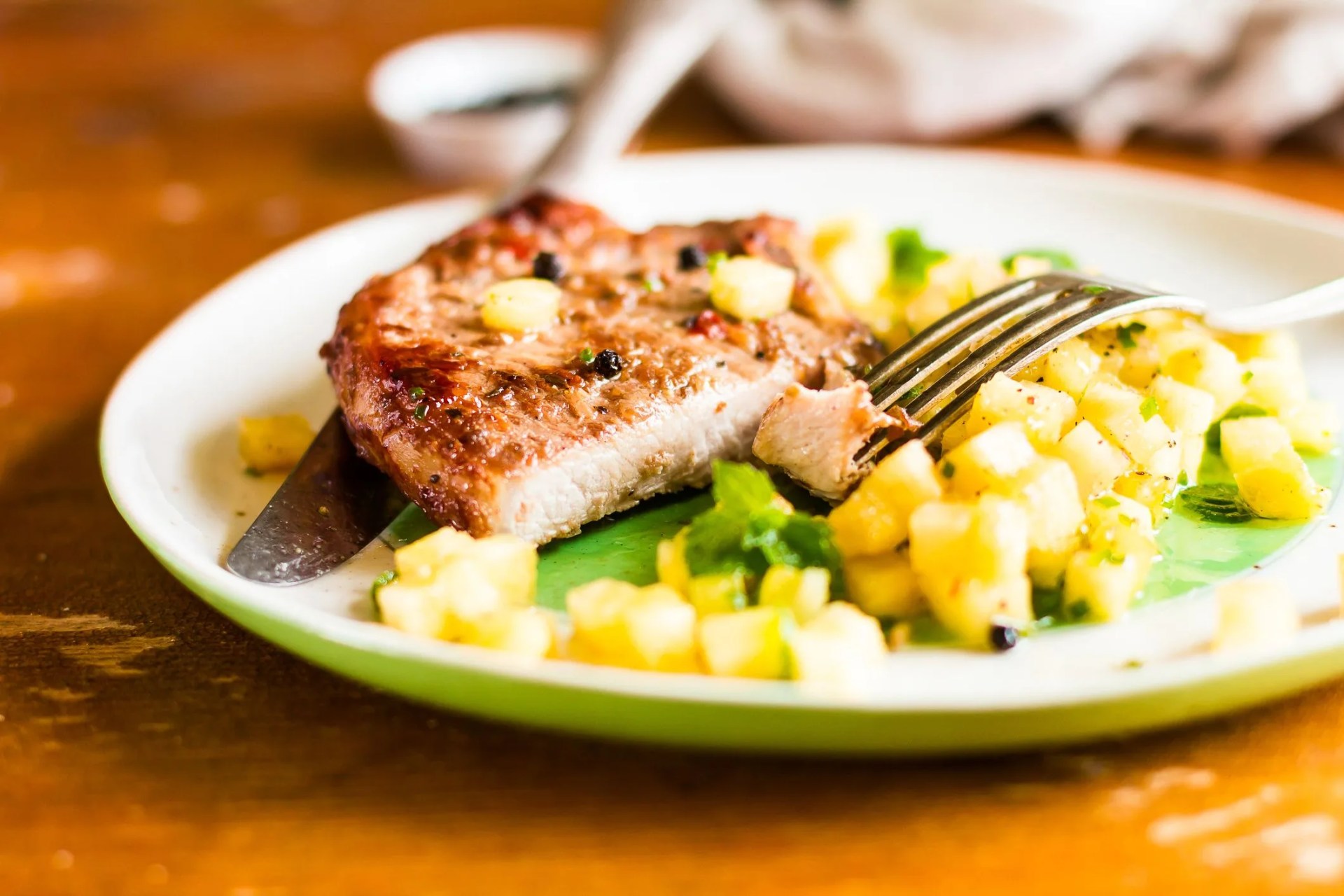 roasted pork chop with pineapple salsa and mint on a plate on a wooden table, selective focus