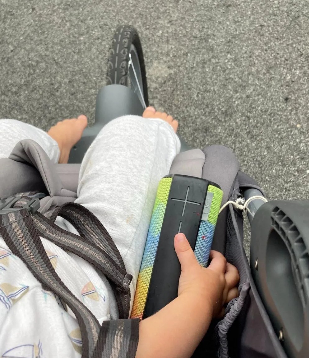 a baby's hand on a bluetooth speaker in a stroller