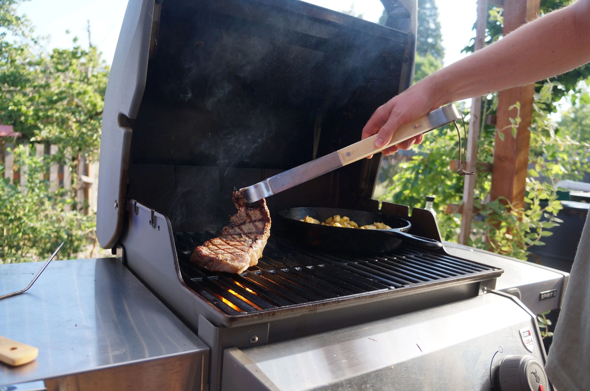 man using grill tongs to flip a steak on a grill