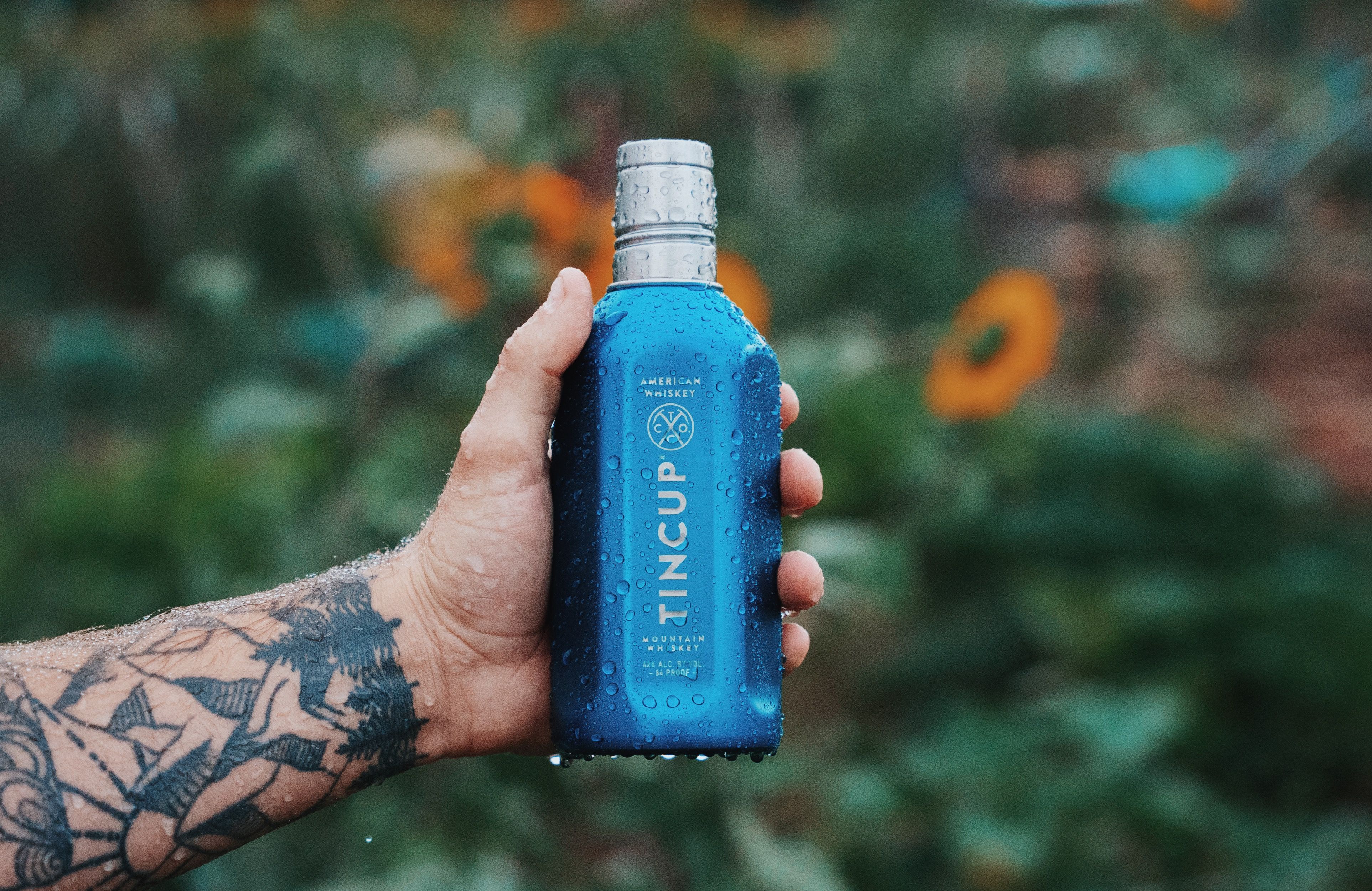 hand with tattoo holding tincup whiskey adventure pack
