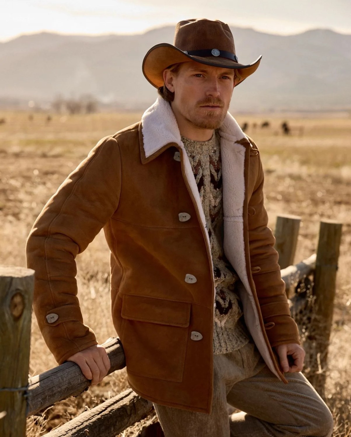 a man in a cowboy hat leaning on a fence with left leg propped up