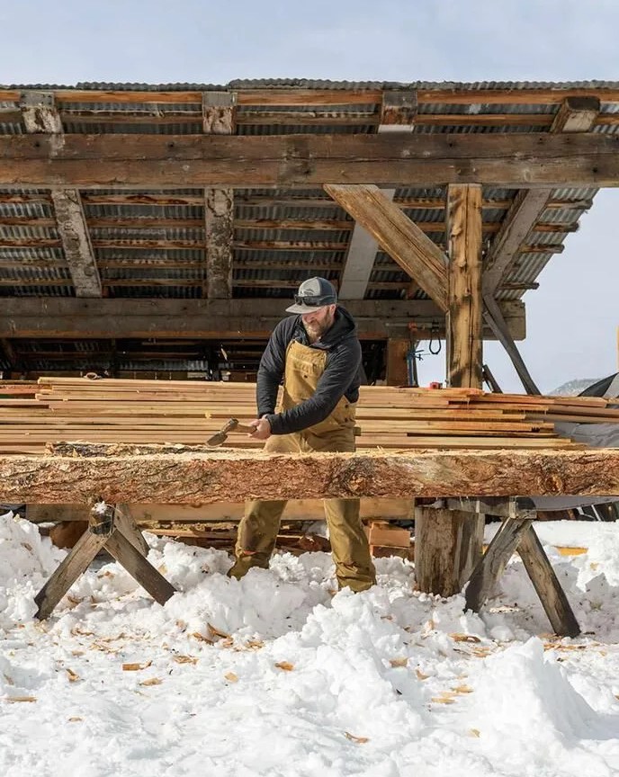 man cutting wood in snowy conditions wearing patagonia workwear hemp tough