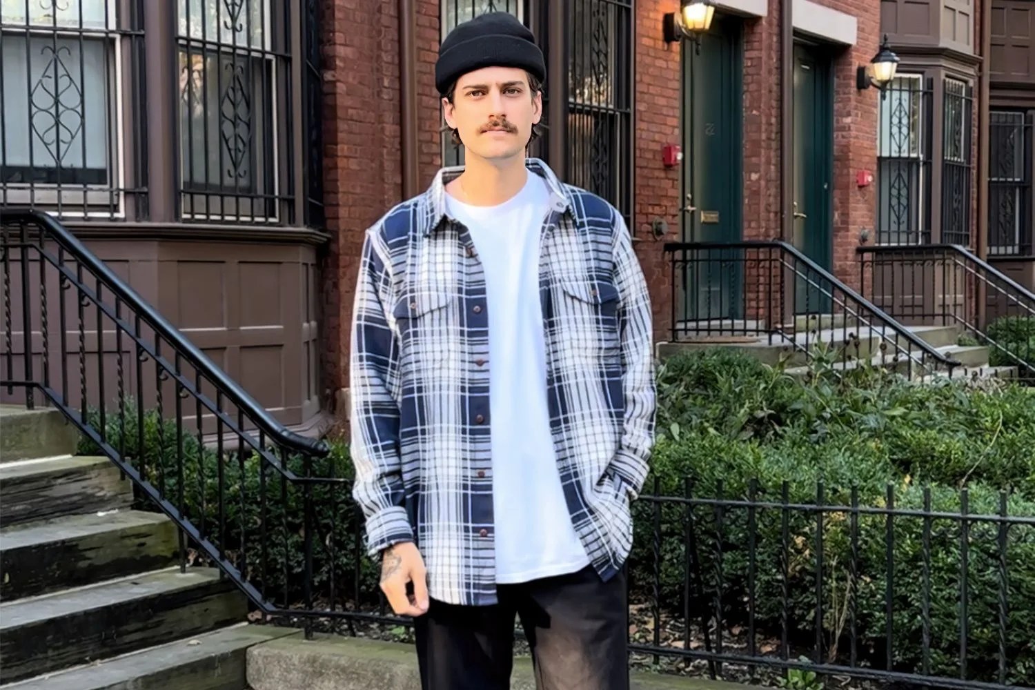 man standing in front of brownstone homes wearing blue and white flannel shirt