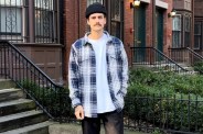 man standing in front of brownstone homes wearing blue and white flannel shirt
