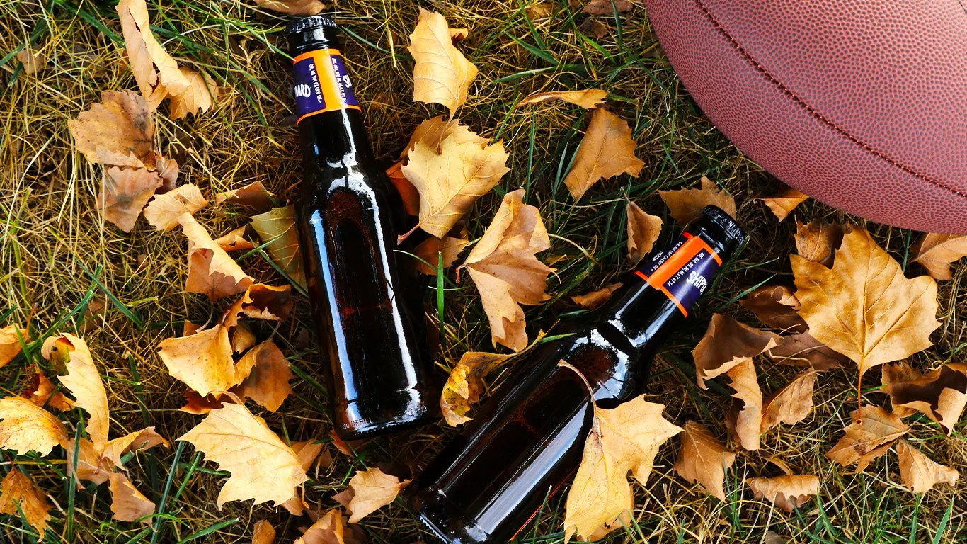 two shipyard pumpkinhead beer bottles on grass next to a football and surrounded by fallen leaves