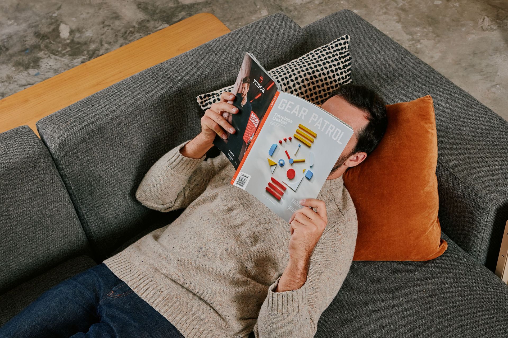 a man laying on a couch reading gear patrol magazine