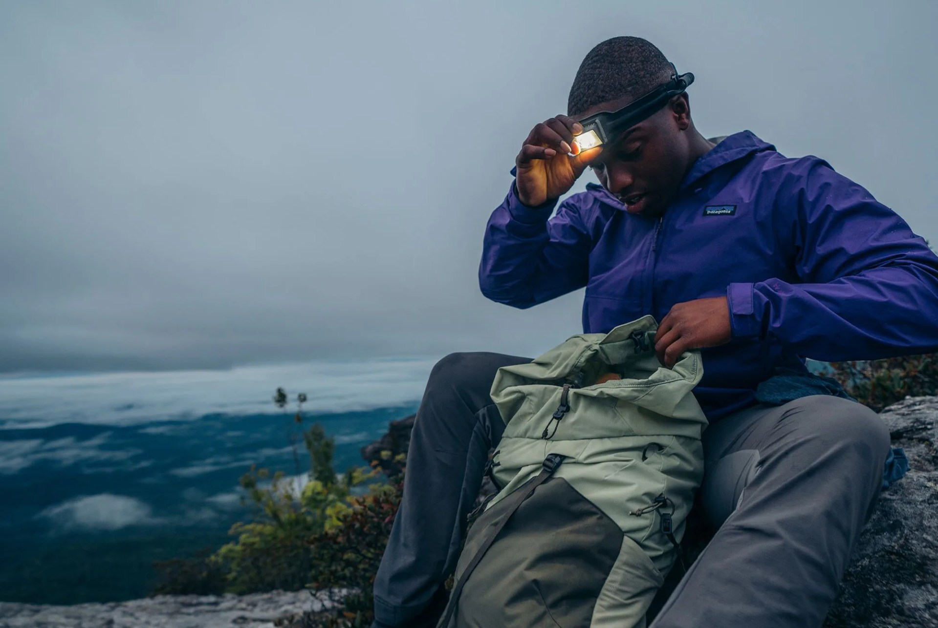 a man sitting on a rock wearing a headlamp and looking into a backpack