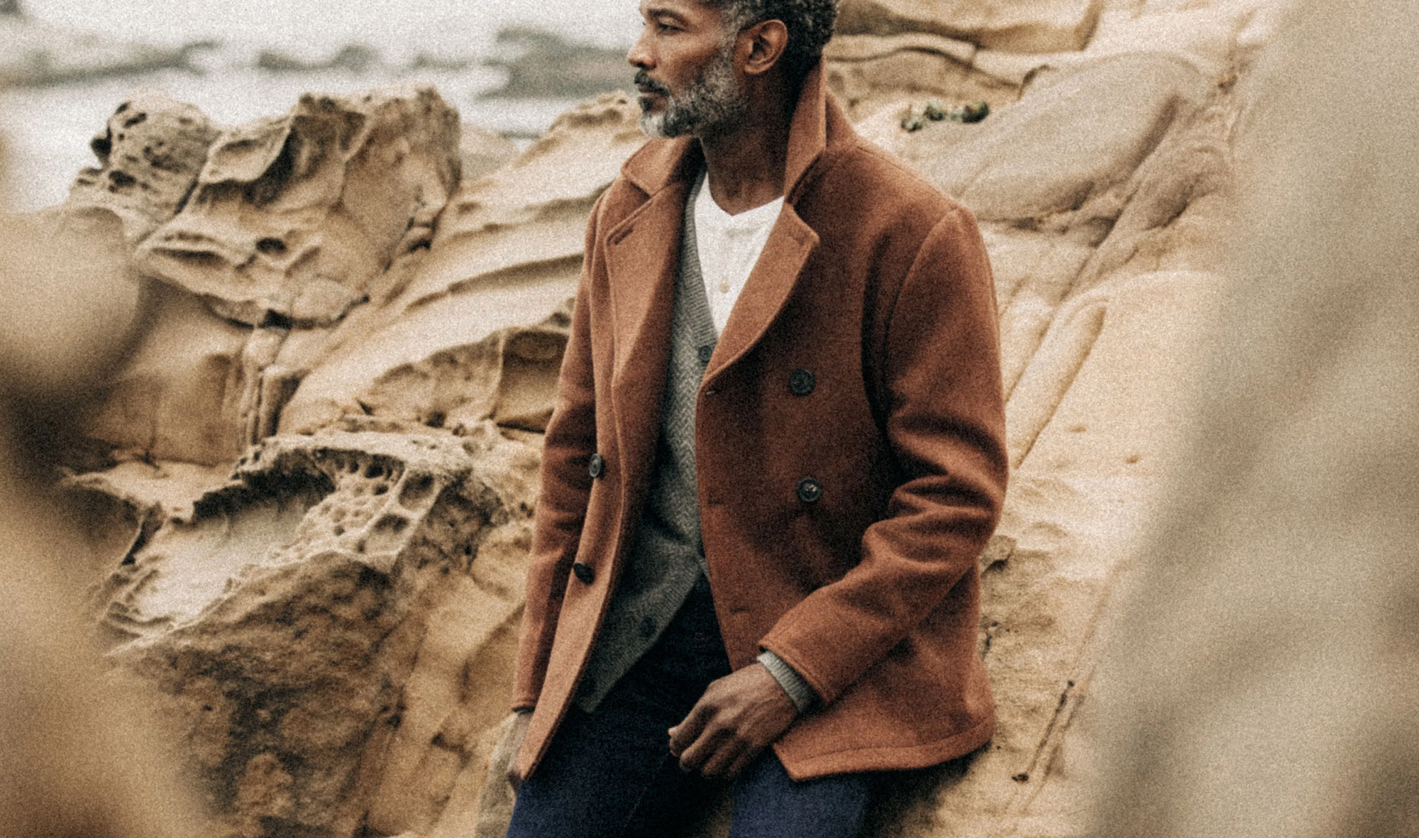 a man on a rocky beach wearing a pea coat