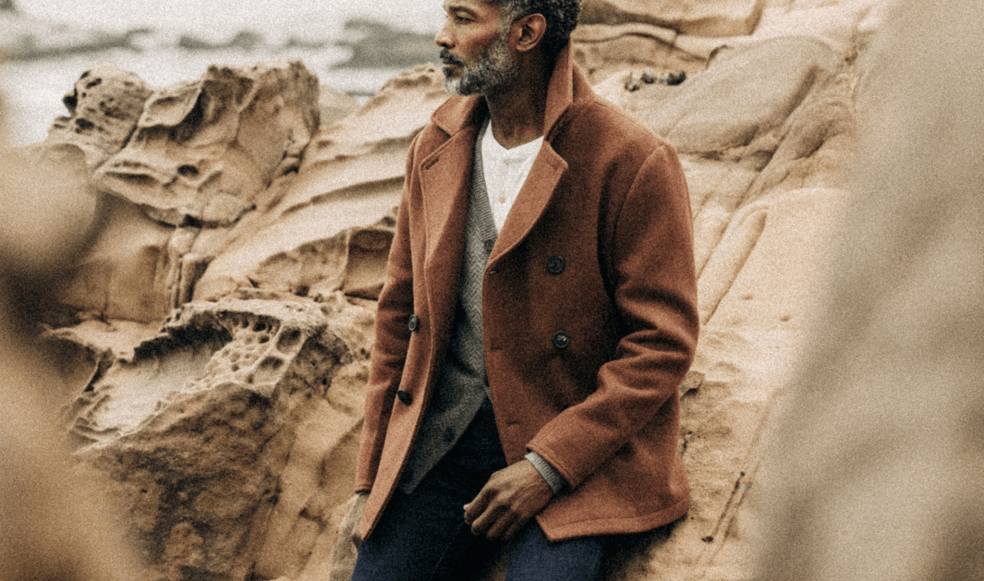 a man on a rocky beach wearing a pea coat