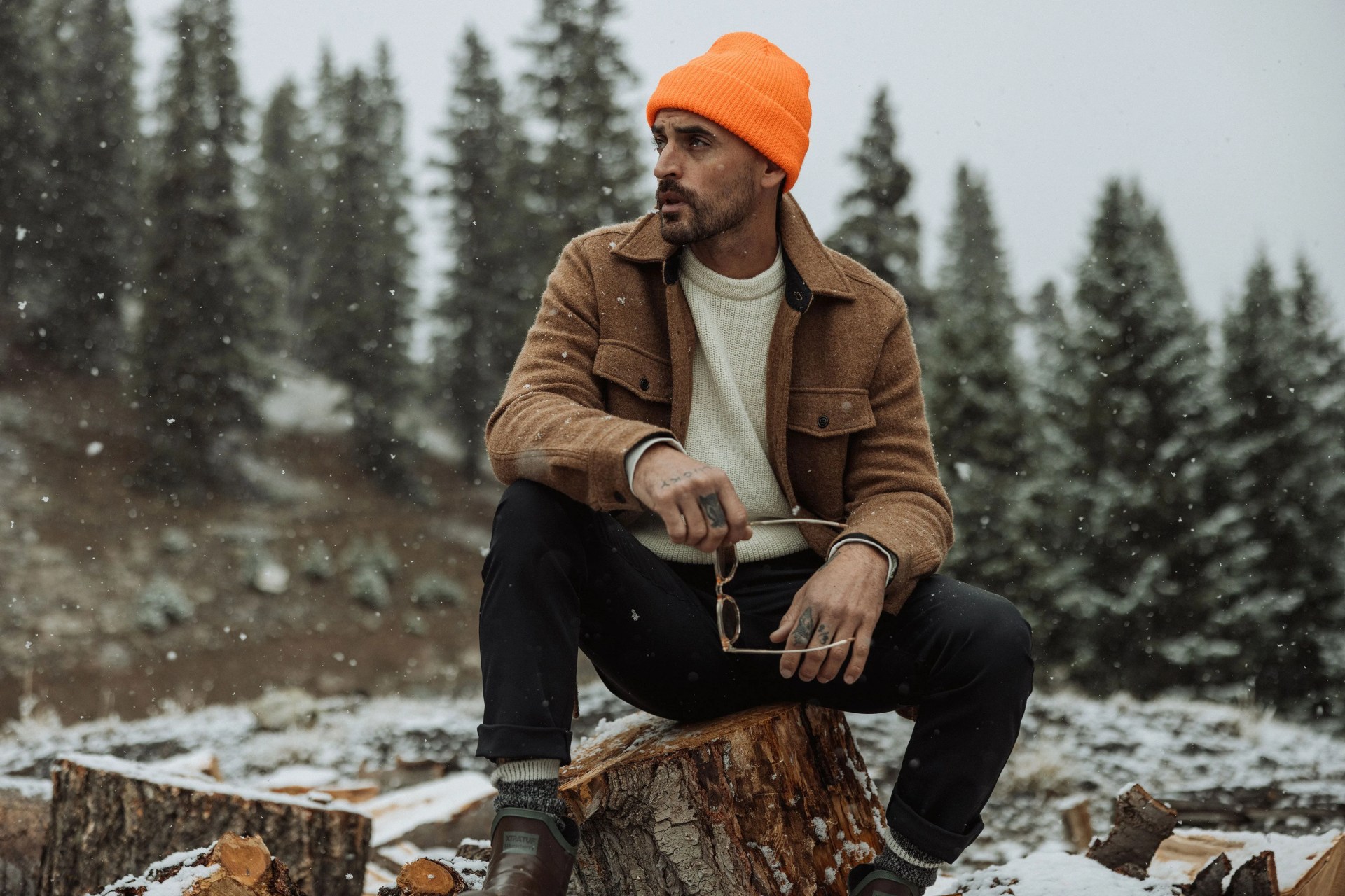 a man sitting on a log holding walden sunglasses
