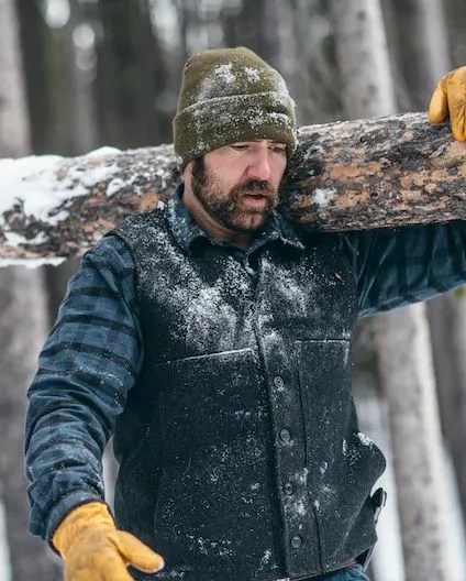 a person holding a branch with snow on it wearing filson mackinaw wool vest