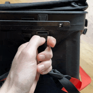 hand pushing on end tab of rux 70 l shoulder strap to detach it from the bags utility rail