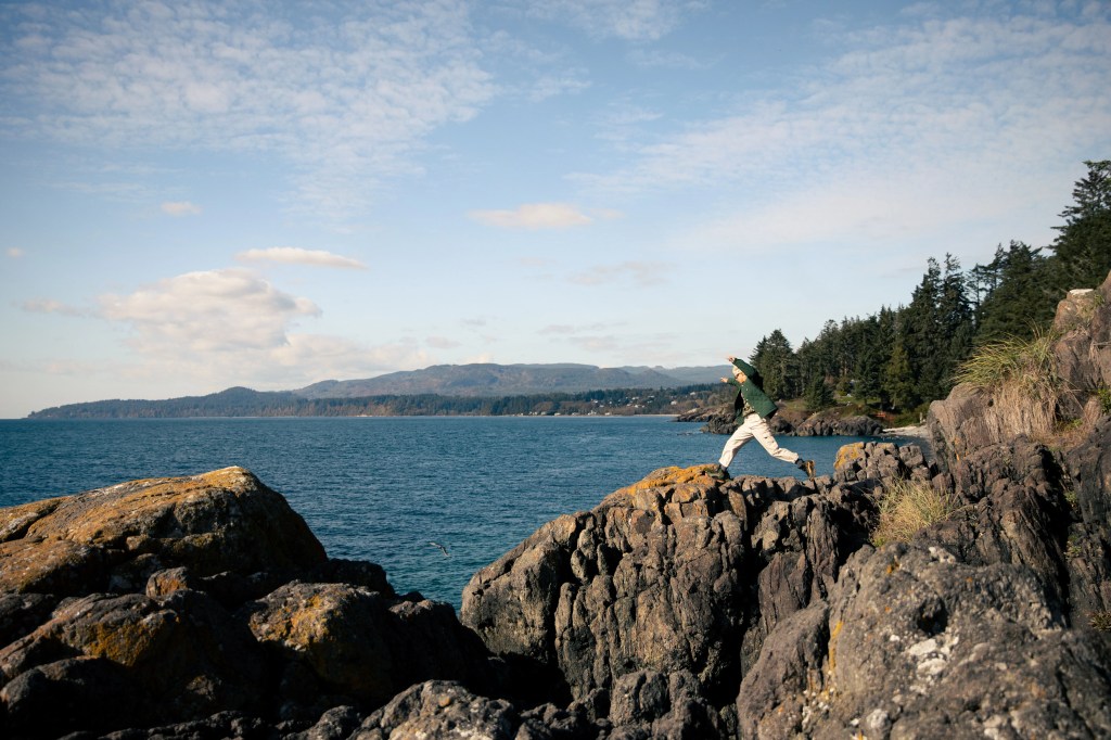hanna scott jumping down a rocky cliffside with the ocean in the back
