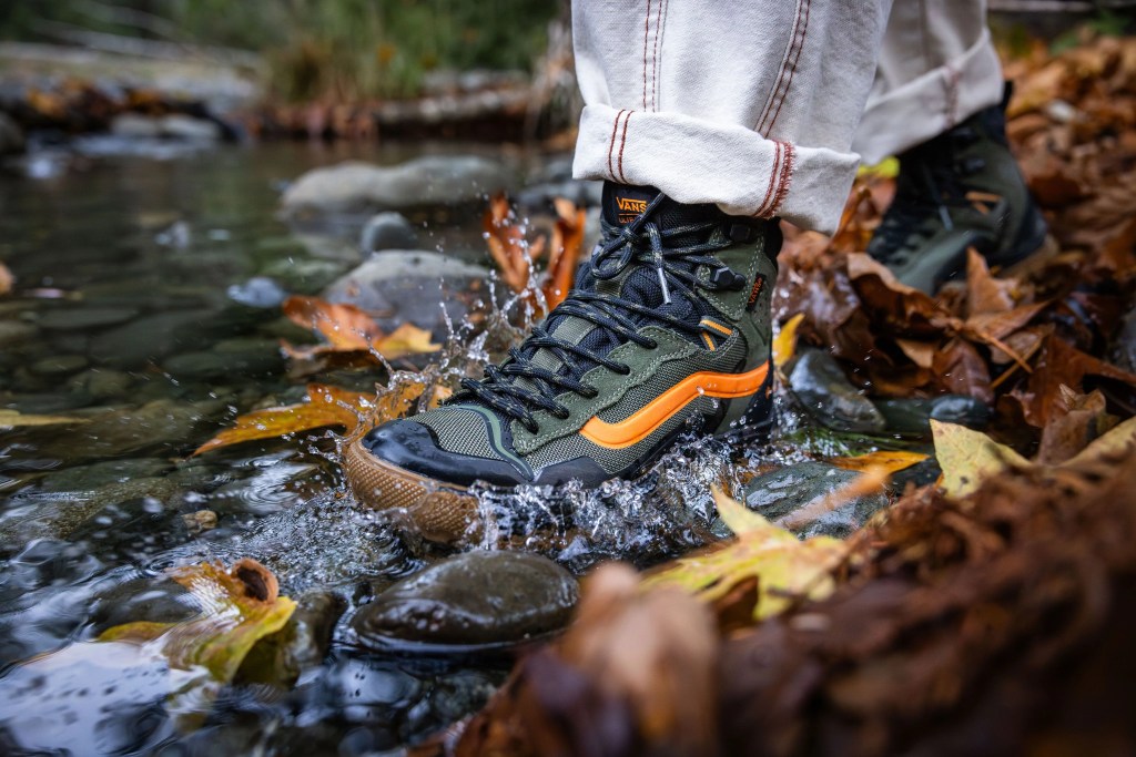a person wearing a pair of vans shoes stepping through creek