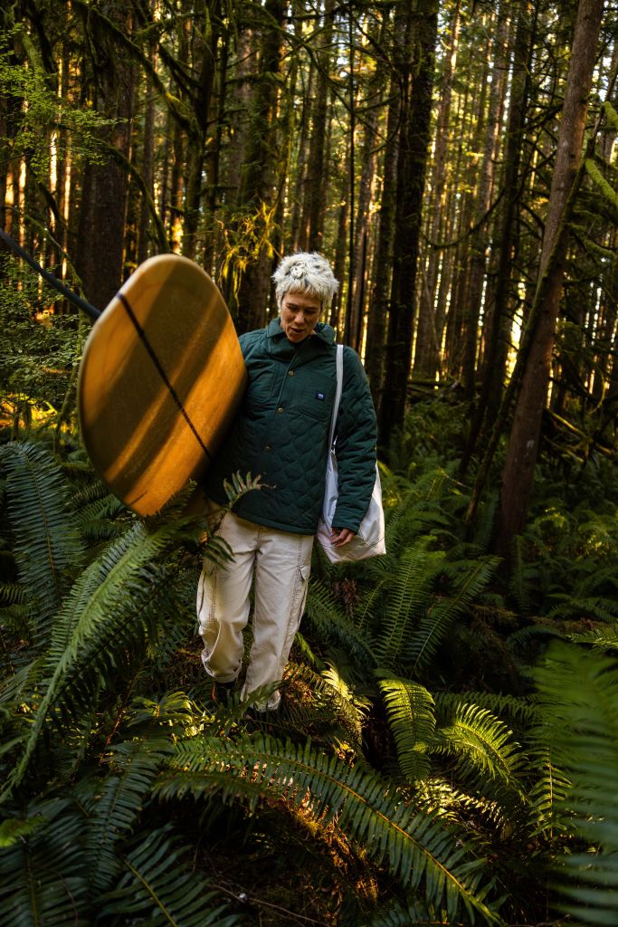 hanna scott walking through forrest carrying surfboard
