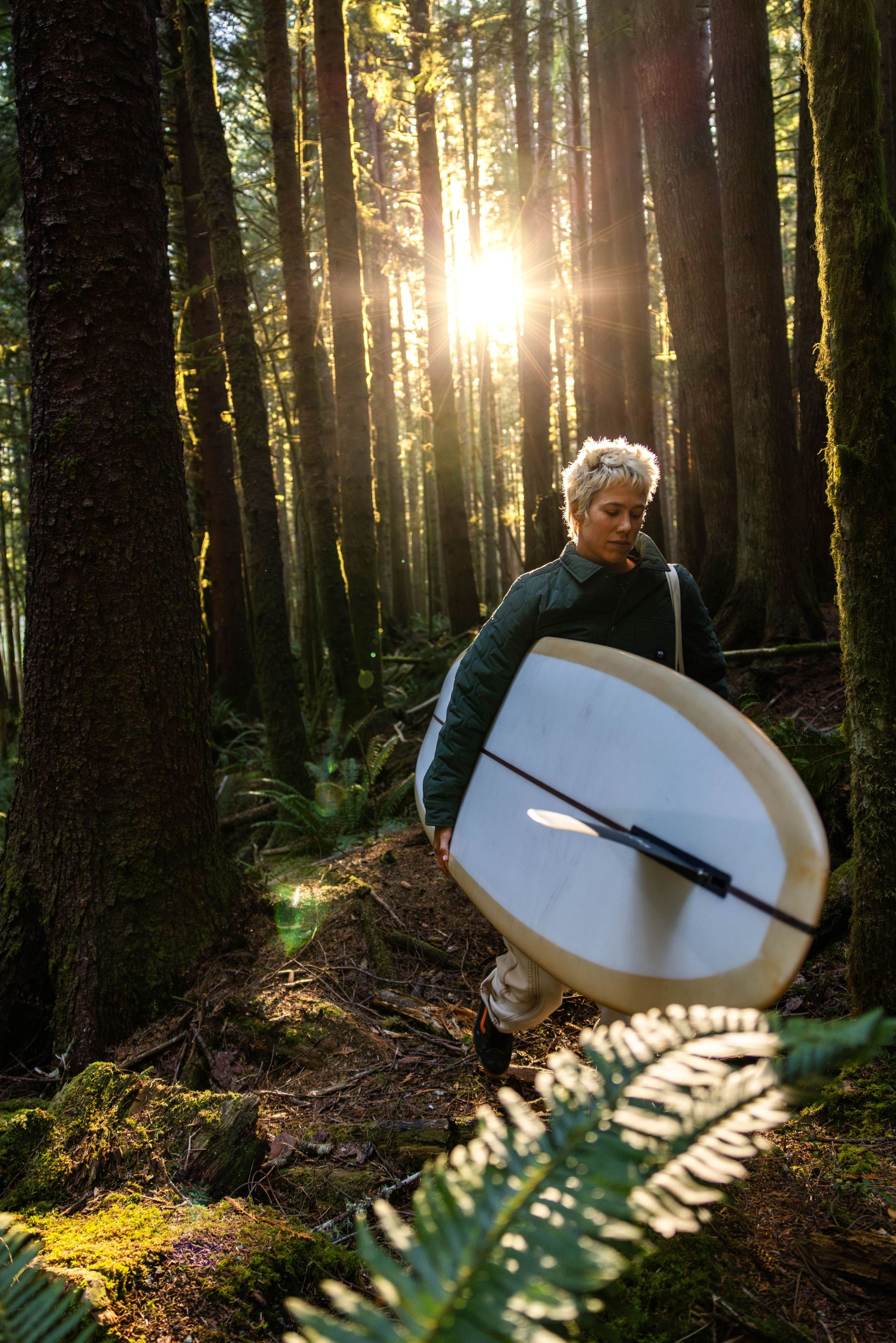hanna scott walking through forrest carrying surfboard